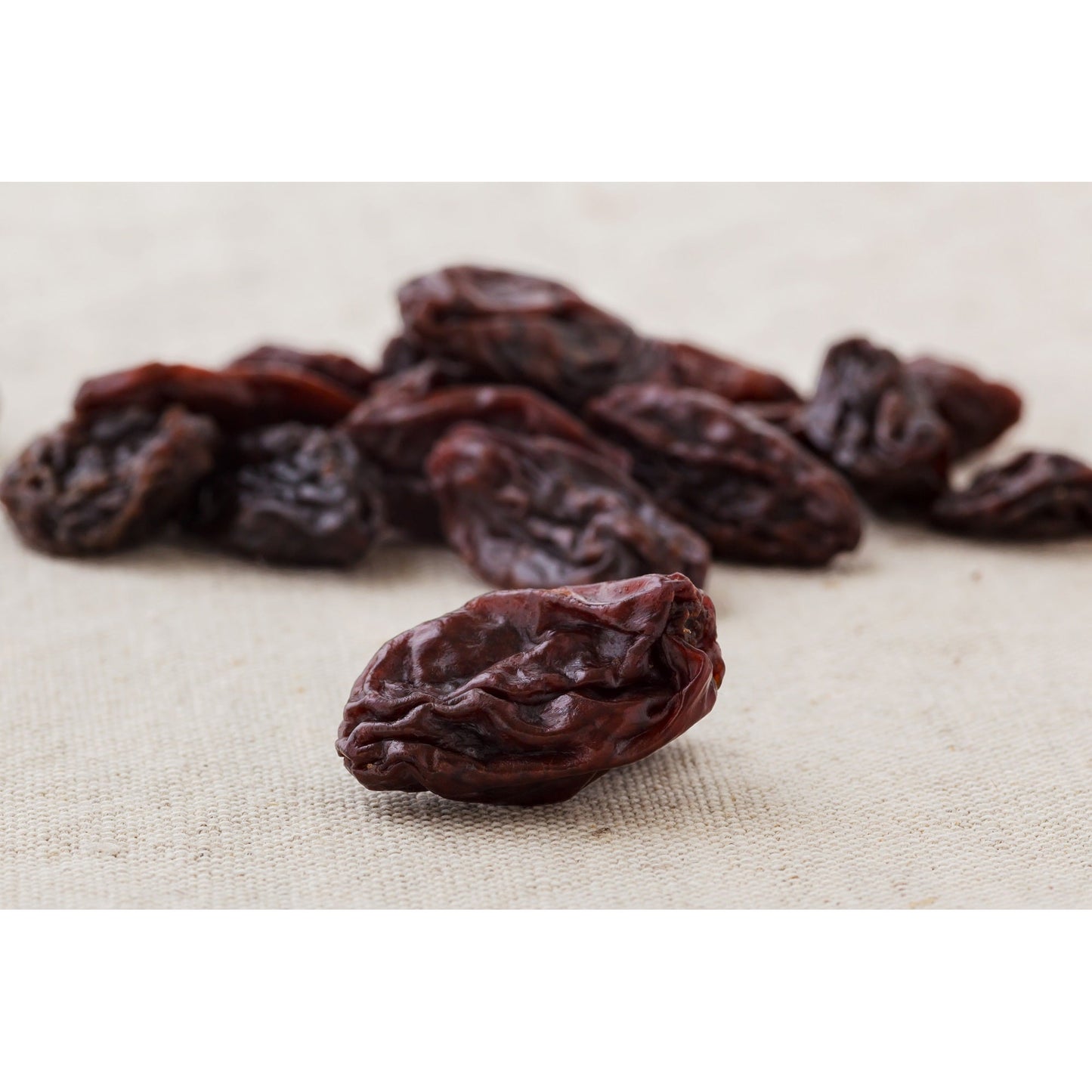 Einzelne weinbeeren jumbo leicht geölt im Vordergrund auf hellem Stoff, weitere Früchte unscharf im Hintergrund, geeignet als Snack oder für Frühstück.