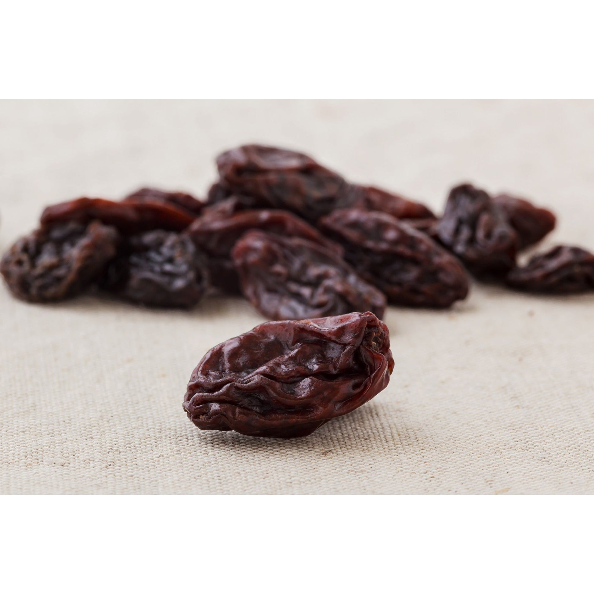 Einzelne weinbeeren jumbo leicht geölt im Vordergrund auf hellem Stoff, weitere Früchte unscharf im Hintergrund, geeignet als Snack oder für Frühstück.
