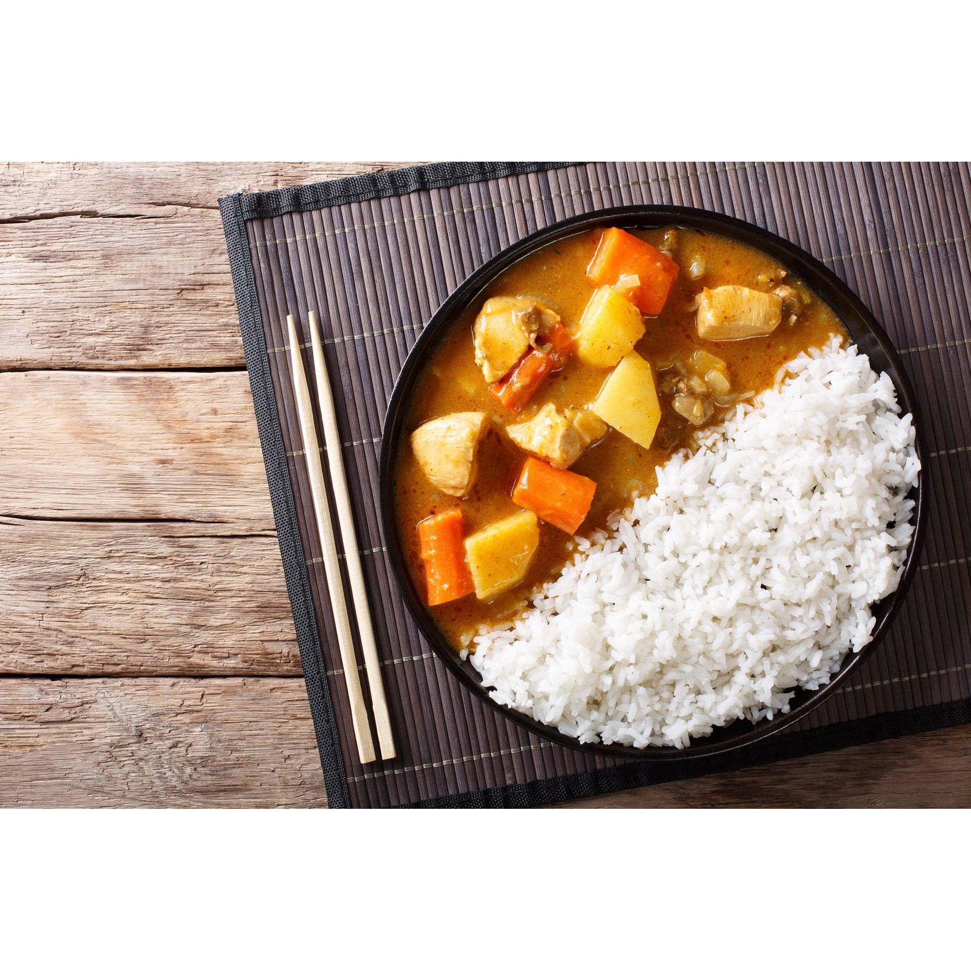 Schale mit Reis und Currygericht, serviert auf einer Bambusmatte mit Essstäbchen, als Inspiration für Curryliebhaber und Freunde von veganen Feinkost-Sets.