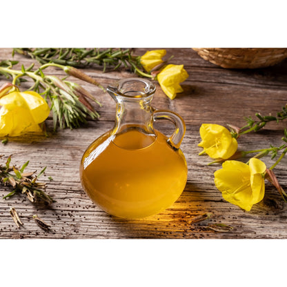 Runde Glaskaraffe mit hochwertigem Nachtkerzenöl auf rustikalem Holztisch, umgeben von Nachtkerze-Blüten und grünen Stängeln.