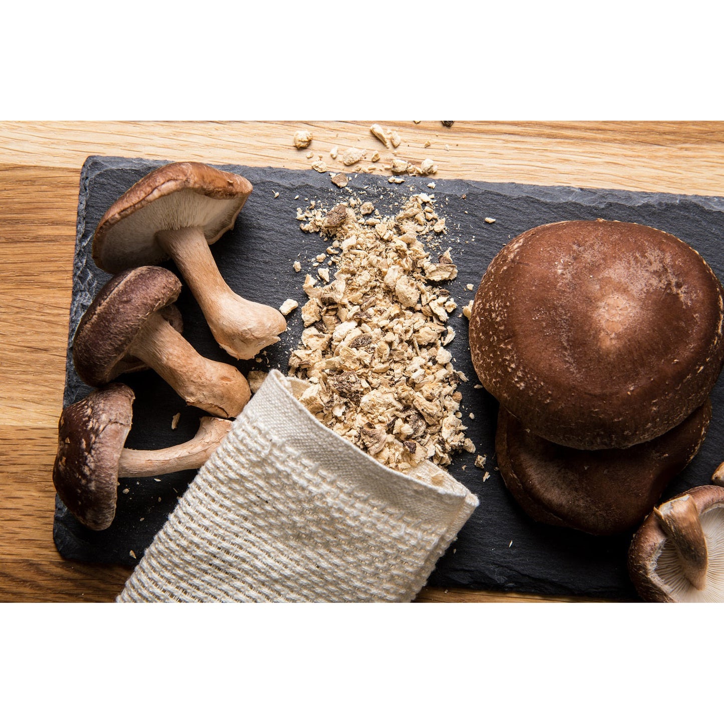 Frische shiitake pilze und zerkleinerte pilzstücke auf einer dunklen Schieferplatte, daneben ein Stoffbeutel.