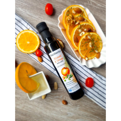 Flasche Fruchtwerker Olivenöl + Orange 250ml auf Holz, daneben Orangenscheiben, Nüsse, Tomaten und ein Schälchen mit Öl und Orangenscheibe, geeignet zum Kochen.