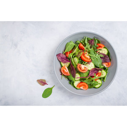 frischer Salat mit Gurken, Tomaten und Blättern, angerichtet in einer Schale, daneben einzelne Blätter als Topping-Idee