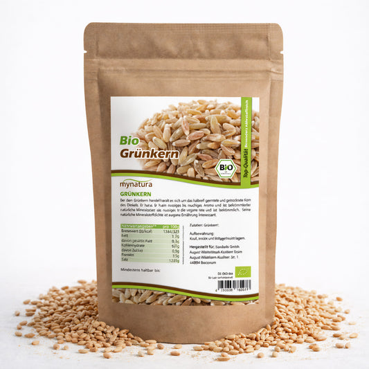 Beutel mit Bio Grünkern ganz von Mynatura, 500g, auf weißem Untergrund, umgeben von losen Getreidesaat-Körnern.