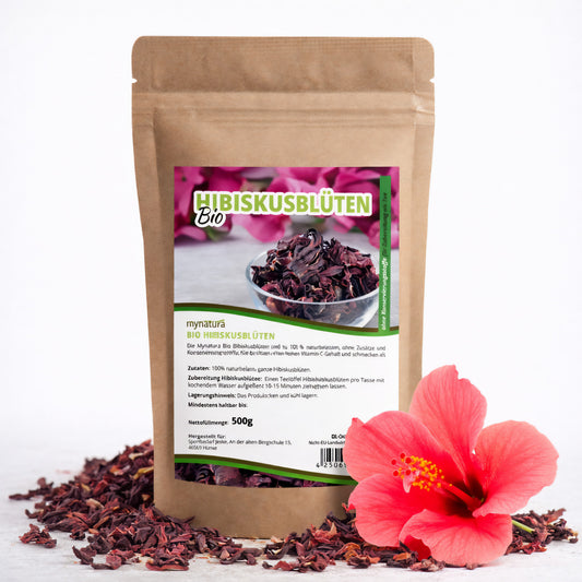 Beutel Mynatura Bio Hibiskusblüten getrocknet, ganz 500g vor weißem Hintergrund mit losen hibiskusblüten und einer frischen Hibiskusblüte daneben.