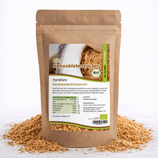Beutel mit mynatura Bio Kokosblütenzucker steht auf verstreutem Kokosblütenzucker, Vorderseite mit Etikett und Nährwertangaben sichtbar.