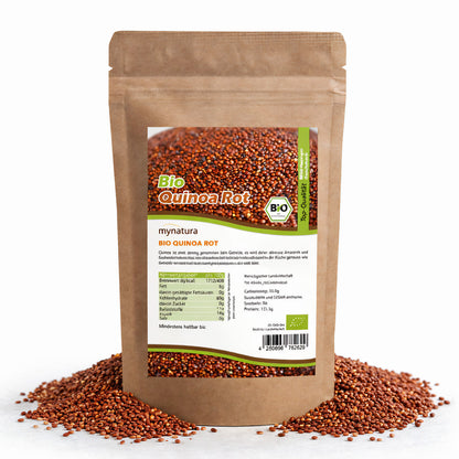 Beutel rotes Bio Quinoa von Mynatura, stehend auf einer Schicht Quinoa-Kerne, Vorderseite mit Etikett und Nährwertangaben sichtbar.