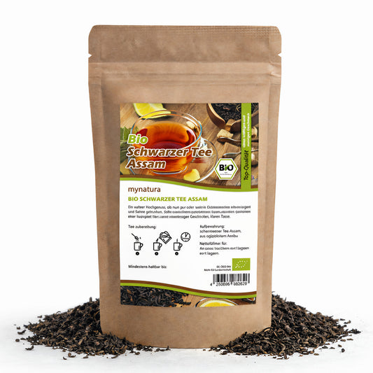 Beutel mynat Assamtee mit Etikett, umgeben von losem kräftigem Schwarztee aus Indien, 100g Packung auf weißem Hintergrund.