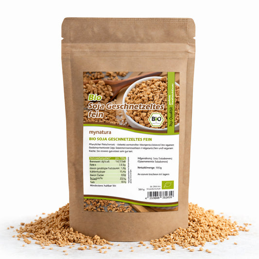 Beutel Mynatura Bio Soja Geschnetzeltes fein mit Sichtfenster auf Sojagranulat, umgeben von verstreutem Sojaprotein auf weißem Hintergrund.