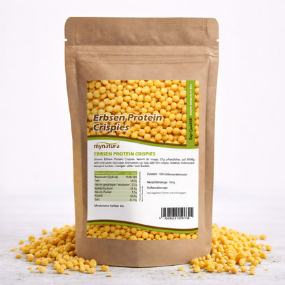 Beutel mit Mynatura Erbsenprotein Crispies 1000g, stehend auf weißem Untergrund, einige Crispies liegen verstreut daneben, Etikett mit Nährwertangaben sichtbar.