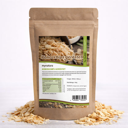 Beutel mit gerösteten Kokoschips von Mynatura, stehend auf einer Unterlage aus verstreuten Kokoschips, Rückseite mit Nährwertangaben sichtbar.