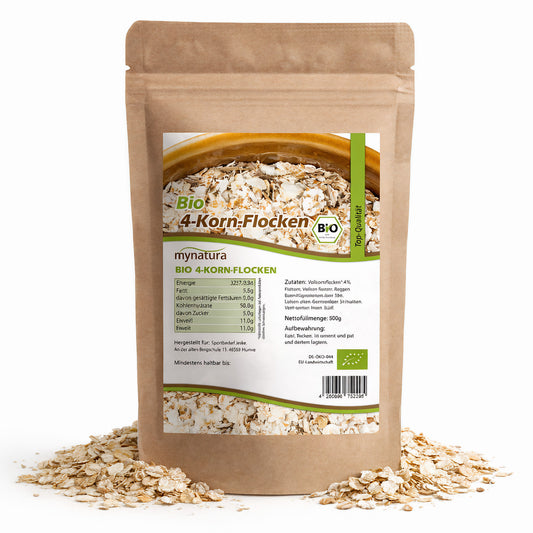 Beutel mit mynatura Bio 4-Korn-Flocken 500g, stehend auf verstreuten Getreideflocken, Vorderseite mit Etikett und Nährwertangaben sichtbar.