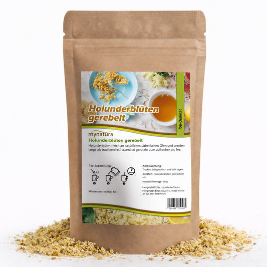 Beutel mit gerebelten Holunderblüten von Mynatura, 100g, stehend auf verstreuten aromatischen Blüten, Vorderseite mit Etikett und Zubereitungshinweisen sichtbar.