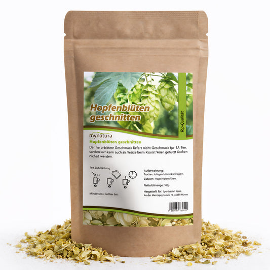 Beutel mit Hopfenblüten geschnitten 100g von Mynatura, stehend auf einer Unterlage aus getrockneten hopfenblüten, Vorderseite mit Etikett und Zubereitungshinweisen sichtbar.