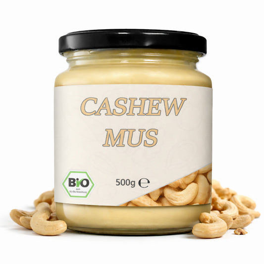 Ein Glas Cashewmus mit schwarzem Deckel und 500g Inhalt, umgeben von Cashewnüssen, als cremiges Nussmus für vegane Küche.
