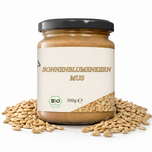 Ein Glas cremiges Sonnenblumenkernmus mit 500g Inhalt, umgeben von Sonnenblumenkernen auf weißem Hintergrund.