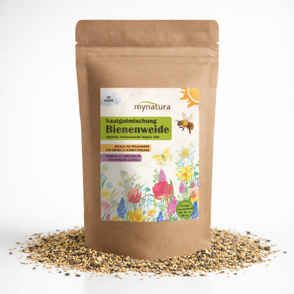 Beutel Mynatura Bienenweide mit 50g Blumensamen, stehend auf verstreuten Samen, Vorderseite mit bunter Blumenillustration und Bienenmotiv.