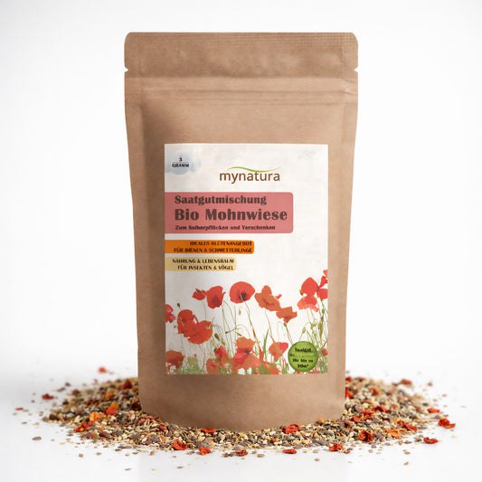 Beutel mit Mynatura Bio Mohnwiese Saatgutmischung, stehend auf verstreuten Blumensamen, Vorderseite mit Etikett und Mohnblumenmotiv.