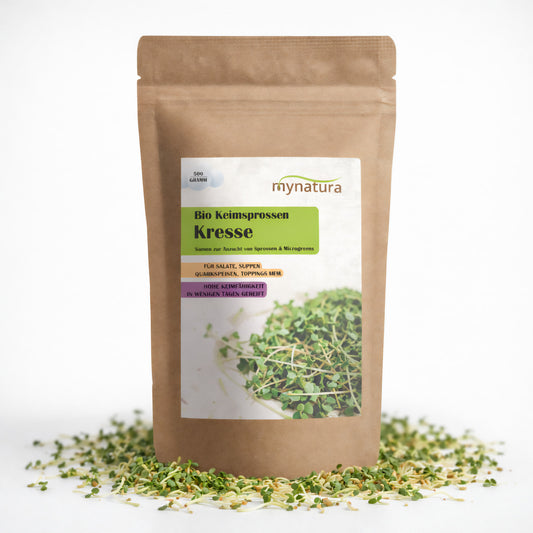 Beutel mit Mynatura Bio Kresse Keimsprossen 500g, stehend auf verstreuten Saaten, Vorderseite mit Etikett und Foto von frischen Sprossen.