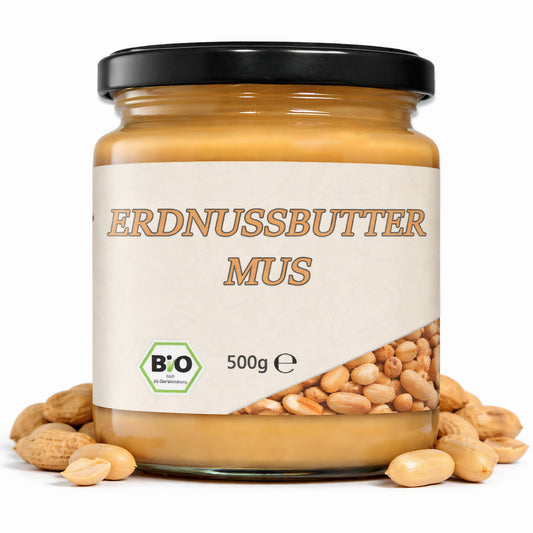 Erdnussbuttermus im 500g Glas mit schwarzem Deckel, umgeben von ganzen und halbierten Nüssen als cremiger Brotaufstrich.