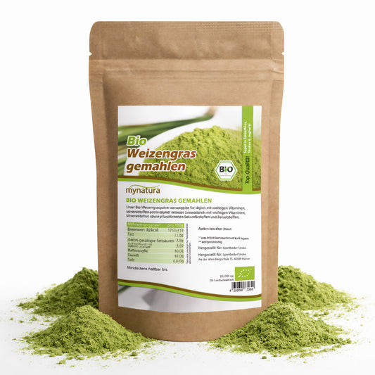 Beutel mit Bio Weizengras gemahlen 500g von Mynatura, stehend auf weißem Hintergrund, umgeben von grünem Superfood-Pulver.