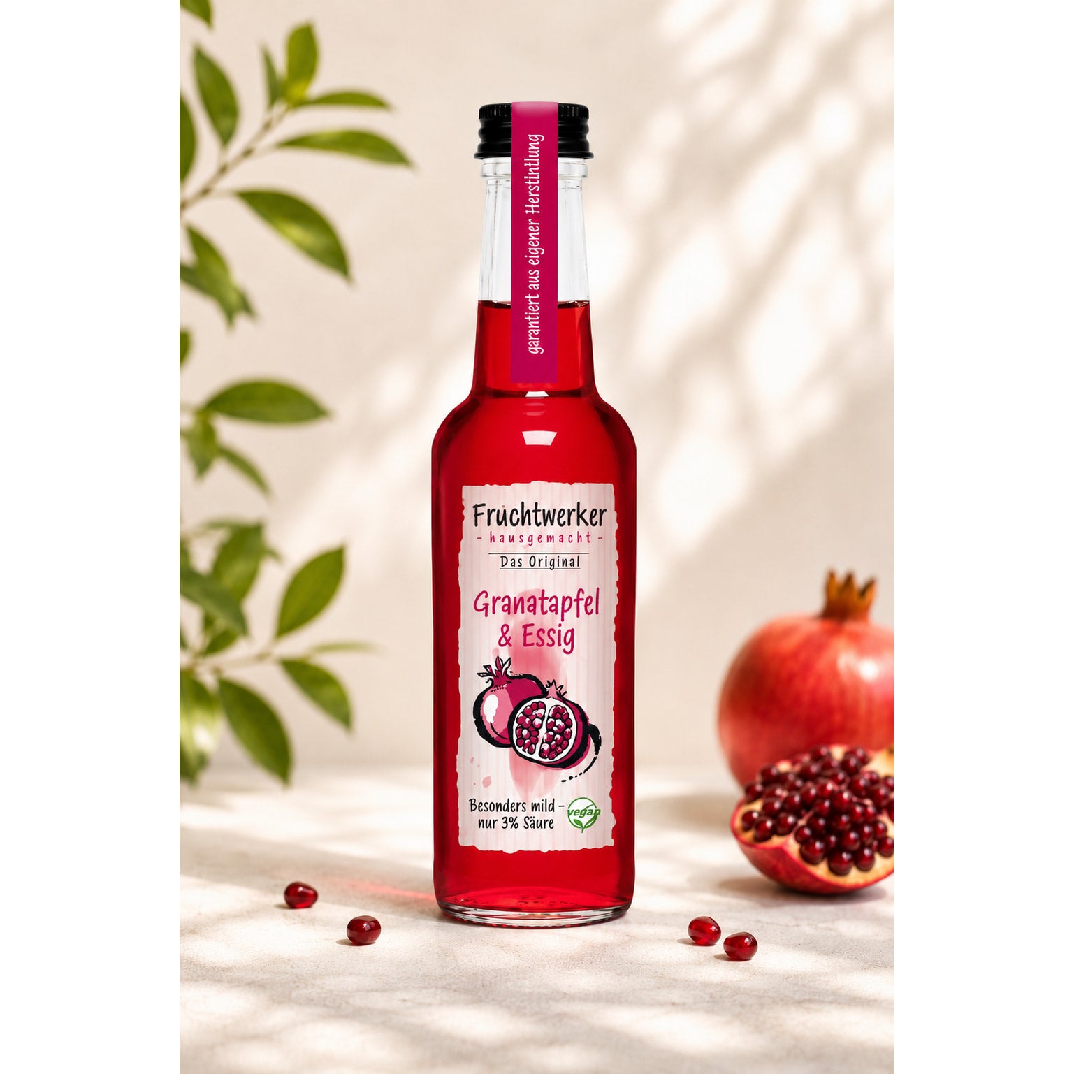 Flasche Fruchtwerker Granatapfel & Essig auf hellem Untergrund, daneben eine aufgeschnittene Granatapfelfrucht und einige Granatapfelkerne.