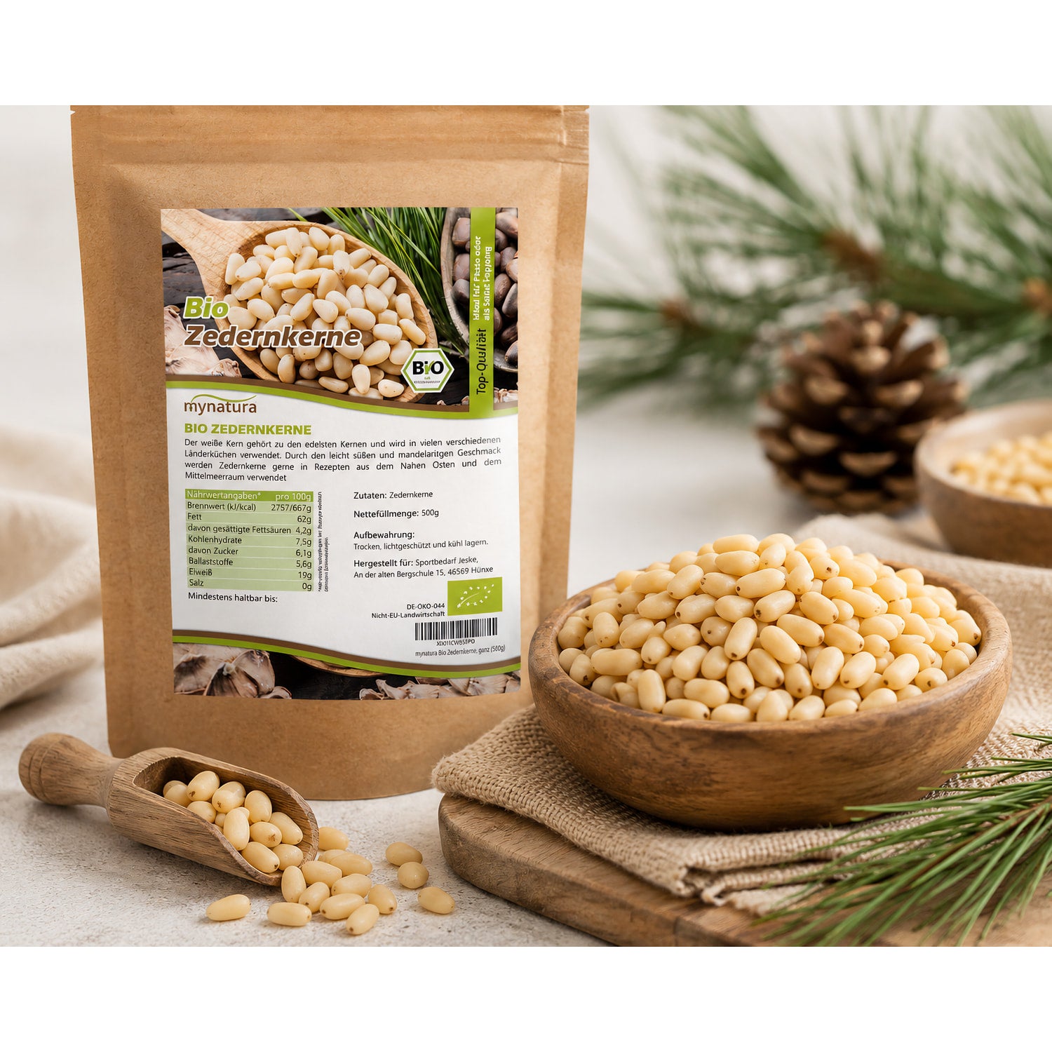 Bio Zedernkerne als Superfood in einer Holzschale und einem Holzlöffel vor dem 500g Beutel, dekoriert mit Kiefernzapfen und grünen Zweigen.