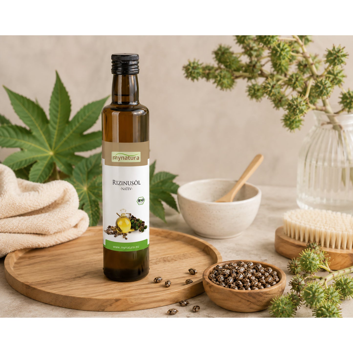 Rizinusöl in Glasflasche auf Holztablett, umgeben von Rizinussamen, Schale, Handtuch, Bürste und grünen Blättern, geeignet für Hautpflege und Kosmetik.