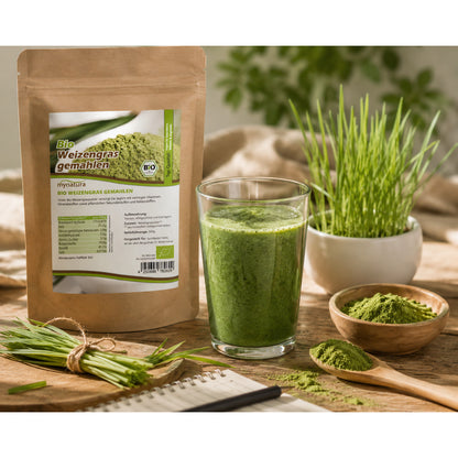 Bio Weizengras gemahlen 500g von Mynatura neben einem Glas grüner Superfood-Getränk, frischem Weizengras und Holzschale mit Pulver auf Holztisch.