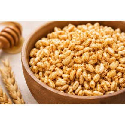 Nahaufnahme einer Holzschale mit gepufftem Dinkel und Honig, daneben Ähren und Honiglöffel, als knuspriger Snack oder fürs Müsli.