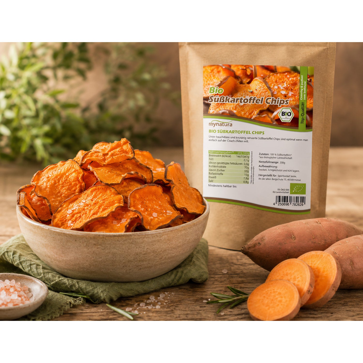 Schale mit knusprigen süßkartoffelchips als snack, daneben Beutel Bio süßkartoffelchips, frische süßkartoffel und Kräuter im Hintergrund