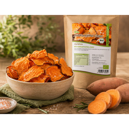 Schale mit knusprigen süßkartoffelchips als snack, daneben Beutel Bio süßkartoffelchips, frische süßkartoffel und Kräuter im Hintergrund