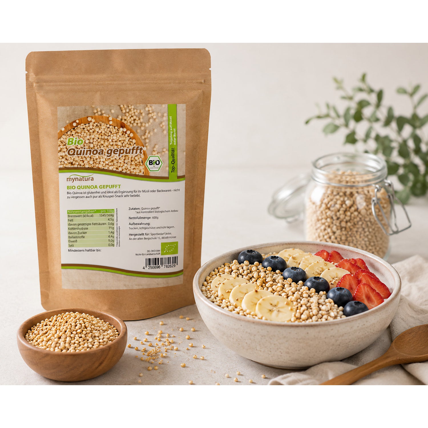 Gepuffter Quinoa fürs Müsli, Beutel neben einer Frühstücksbowl mit Früchten und einer Schale Quinoa, im Hintergrund ein Glas mit Quinoa.