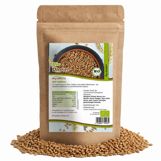 Beutel mit Bio Dinkel ganz von mynatura, 500g, stehend auf einem Haufen Dinkelkerne, Vorderseite mit Nährwertangaben und Zutaten gut lesbar.