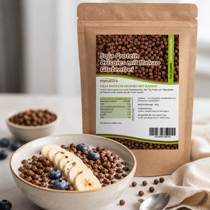 Soja Protein Crispies mit Kakao im Beutel von Mynatura, im Hintergrund eine Schale mit Müsli, Bananenscheiben und Blaubeeren als Frühstück serviert.