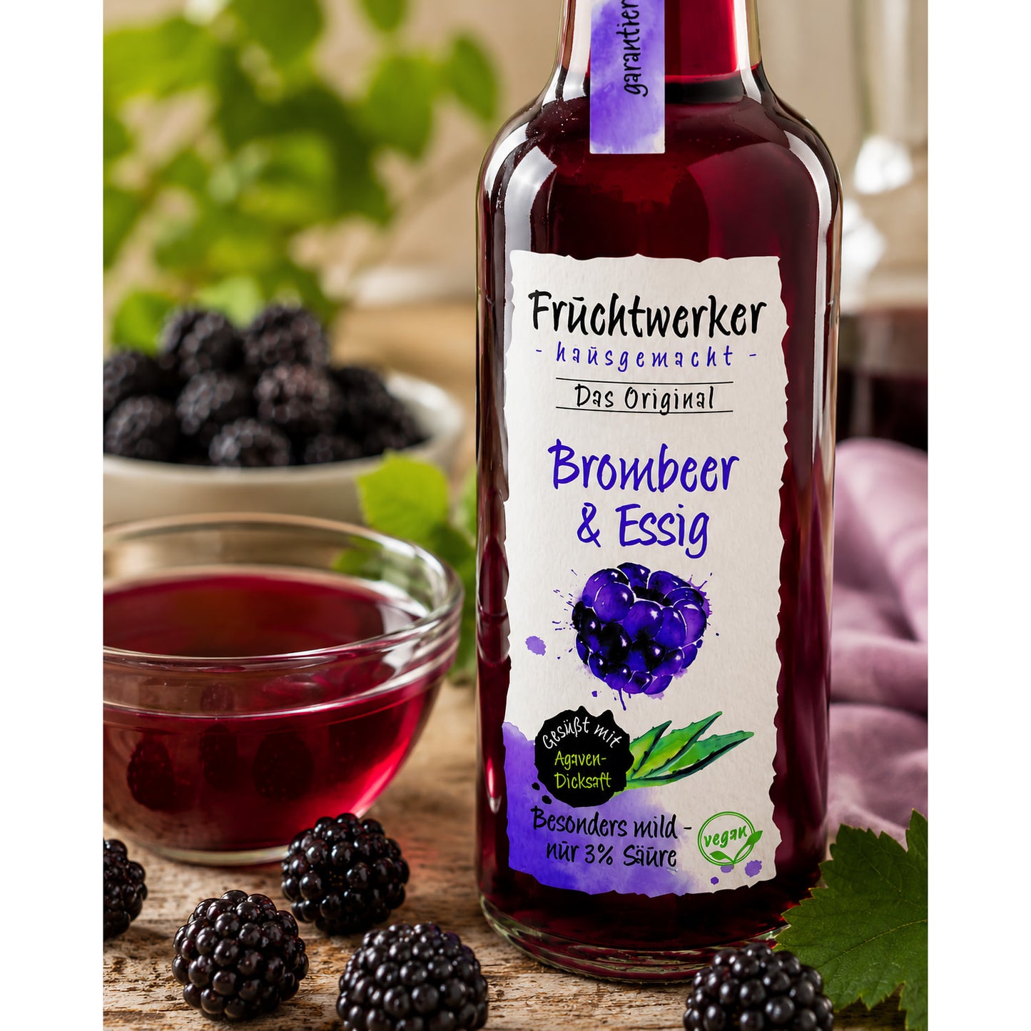 Nahaufnahme der Flasche Fruchtwerker Brombeer & Essig auf Holztisch, daneben frische Brombeeren und eine Schale mit Essig.