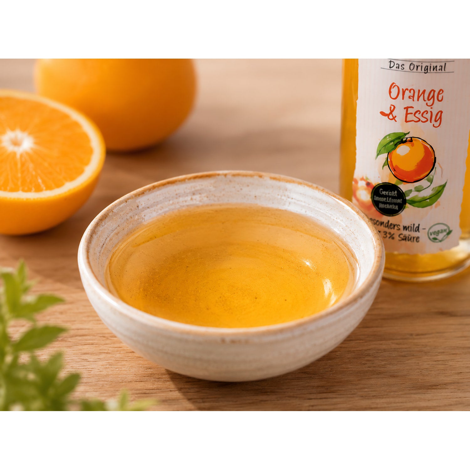 Keramikschale mit orangefarbener Flüssigkeit, daneben eine angeschnittene Orange und ein Teil der Flasche Fruchtwerker Orange & Essig.