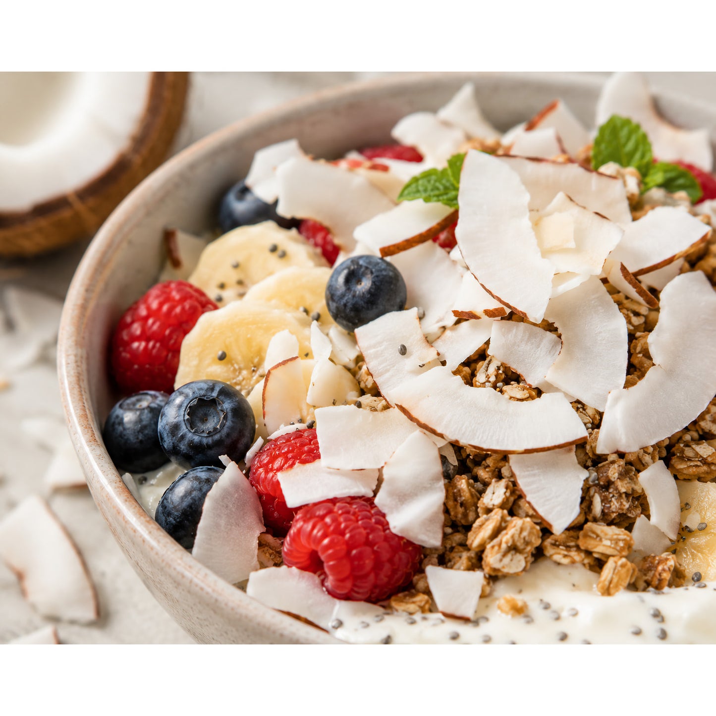 Frühstücksschale mit Kokoschips, frischen Früchten wie Himbeeren, Blaubeeren, Bananen und Granola, als Superfood-Topping für Snacks oder Frühstück.
