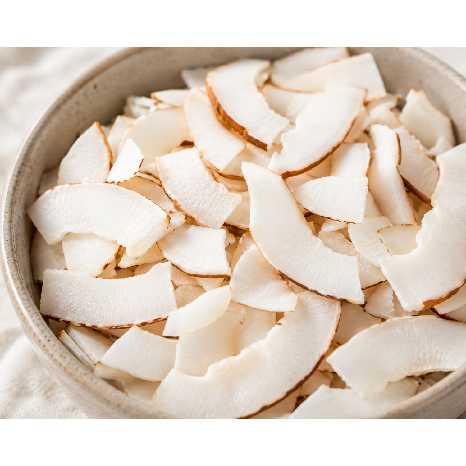 Schale mit naturbelassenen Kokoschips, die als vegane Früchte-Snackalternative serviert werden, Nahaufnahme der knusprigen Kokosstücke.