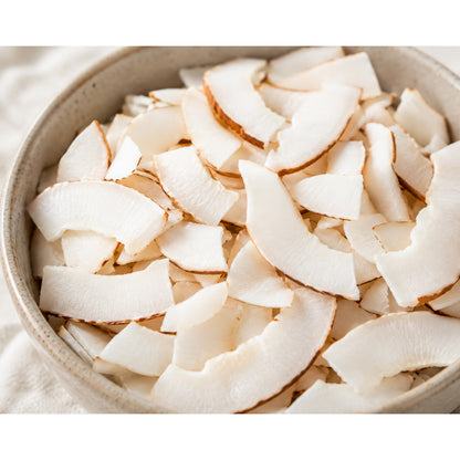 Schale mit naturbelassenen Kokoschips, die als vegane Früchte-Snackalternative serviert werden, Nahaufnahme der knusprigen Kokosstücke.